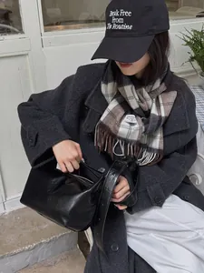 Detalle de bufanda de lana a cuadros marrón con bolso de hombro de cuero plisado en negro