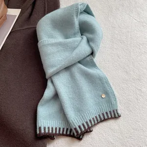 Detail of wool blend scarf featuring soft knit texture and golden metal logo charm