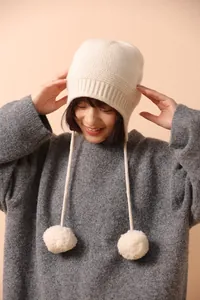 Detalle del gorro de lana crema con orejeras, pompones grandes y textura de canalé