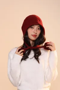 Detail of dark red knit pumpkin hat with ear flaps and decorative pom-poms on the ties