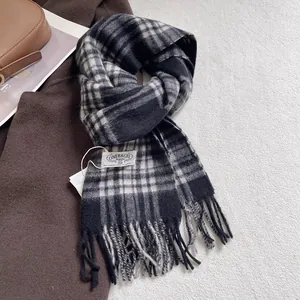 Detail of wool scarf showing plaid pattern, fringe edges and sewn brand label on coat