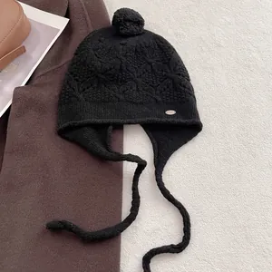 Close-up of black wool crochet hat showing hollow diamond pattern and metal logo plate