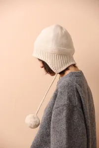 Detalle de gorro de lana de punto crema con lazos de pompones y diseño de orejeras