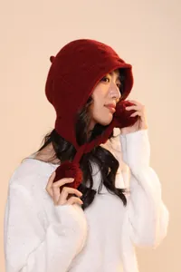 Detail of dark red wool knit trapper hat with cable pattern and plush pompoms