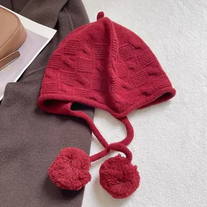 Detailed knit texture of a dark red pumpkin-style bonnet with cute pom-pom ties