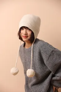 Primer plano del gorro de lana beige con orejeras y detalle de pompón en una modelo