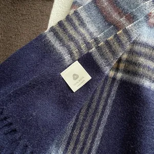 Close-up of 100% wool scarf featuring plaid pattern, fringes and handmade label