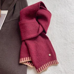 Macro detail of wool blend scarf featuring burgundy knit and golden logo emblem