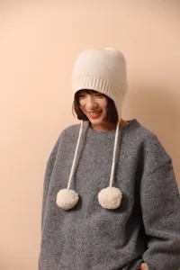 Detalle del gorro de lana crema con pompones y textura acanalada para un estilo cálido de invierno