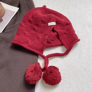 Close-up of red 100% wool knit hat showing warm waffle texture and soft pom-pom ties