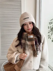 Close-up of a warm 100% wool plaid scarf and a beige knitted beanie on a model