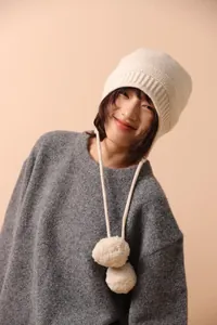 Detalle de la textura de punto del gorro de lana blanco roto con pompones y orejeras