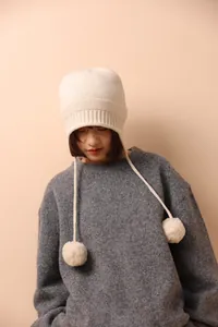 Detalle del tejido y pompones blancos en un gorro de lana de invierno con orejeras