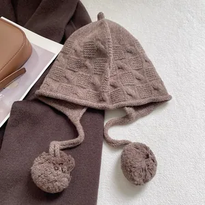 Detailed close-up of brown knit wool hat featuring cable patterns and soft pom-poms