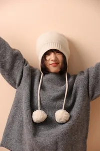 Detalle del tejido de punto y pompones de este gorro de lana blanco crema con orejeras
