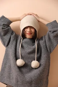 Detalle de la textura de punto de un gorro de lana blanco crema con pompones