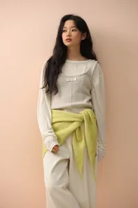 Detail of a bright lime green knit shawl tied around waist over a beige ribbed vest