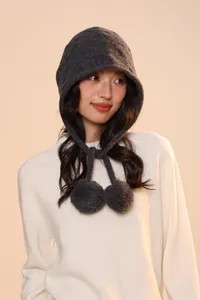 Close-up of dark grey wool knit earflap hat featuring decorative soft plush pom-poms