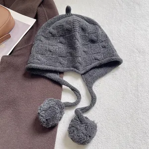 Detail of grey knitted wool beanie featuring soft waffle texture and decorative pom-poms