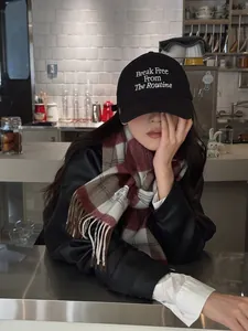 Detalle de bufanda de lana a cuadros rojos y grises con flecos y una gorra negra de algodón