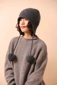 Detalle del gorro de lana de punto con pompones decorativos y correas largas en gris oscuro