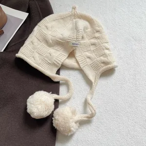 Close-up of cream wool knit hat featuring 100% wool label and soft plush pom poms