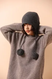 Detalle del tejido de lana del gorro gris oscuro con orejeras y pompones decorativos