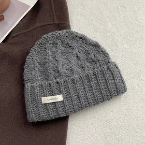 Detail der Strickstruktur einer grauen Wollmütze mit Zopfmuster und 100% Wolle Textiletikett