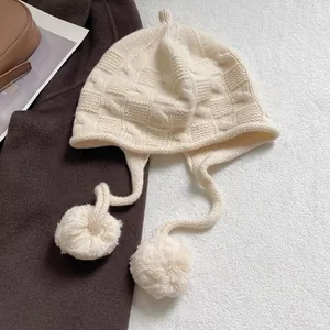 Detailed knit texture of a cream pumpkin-style hat with fluffy pompoms and earflaps