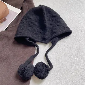 Detail of black knit earflap hat with chunky texture and decorative plush pom-poms