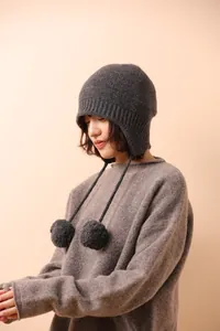 Detalle de gorro de punto gris oscuro con orejeras, pompones y lazos para el invierno