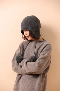 Detalle de gorro de lana gris oscuro con pompones y orejeras para el invierno
