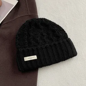 Detail einer schwarzen Strickmütze aus 100% Wolle mit grobem Zopfmuster und weißem Etikett