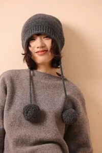 Textura detallada del gorro de lana gris oscuro con cordones decorativos y pompones suaves
