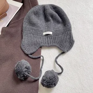 Vista detallada de gorro de punto de lana con orejeras y pompones grises de tacto suave