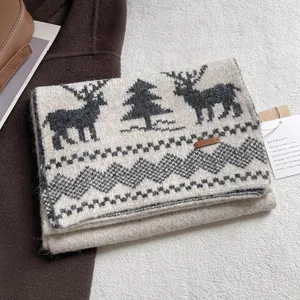 Close-up of beige knitted winter scarf with grey reindeer patterns and leather tag