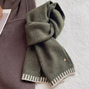 Detail of wool blend knit scarf in dark green with white stripes and a gold logo tag