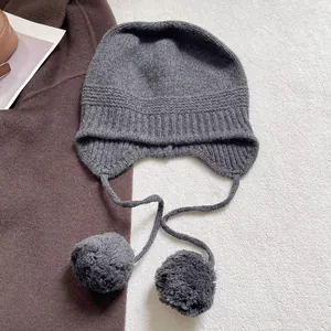 Detalle del gorro de punto de lana gris oscuro con textura acanalada y pompones