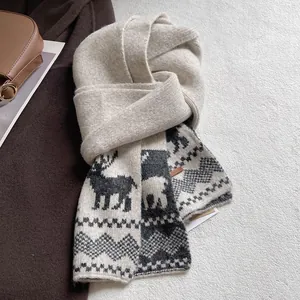 Detail of cream knitted scarf with dark grey reindeer pattern and leather brand logo label