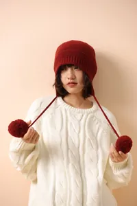 Detalle del gorro de lana roja con orejeras y pompones junto a un jersey de punto blanco