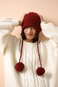 Detalle del tejido de un gorro de lana granate con orejeras y pompones suaves