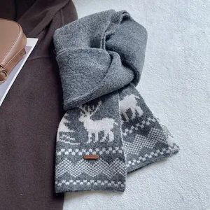Detailed knit texture of a dark grey winter scarf featuring white reindeer and snowflake motifs