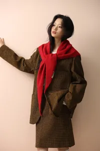 Detailed view of heavy knit red shawl layered over a classic brown plaid wool blazer outfit