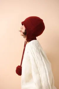 Detalle del gorro de lana de punto rojo oscuro con orejeras, pompones y cordones