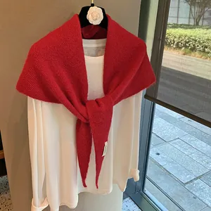 Detail of red knitted shawl tied on a white shirt featuring soft texture and brand label