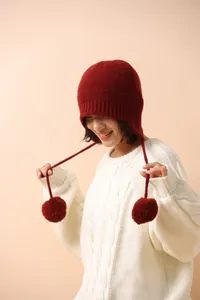 Detalle de gorro de lana de punto con orejeras y pompones de pelo sintético color granate
