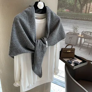 Detail of dark grey 100% wool knitted shawl with brand tag on a neutral indoor backdrop