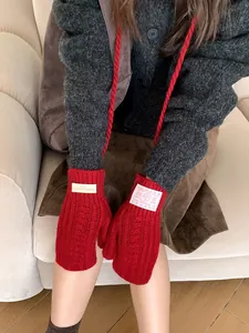 Detail of red cable-knit mittens featuring a hanging rope and decorative cloth labels