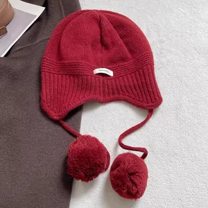 Detalle del gorro de lana roja con textura de canalé y pompones suaves en el lado de la oreja