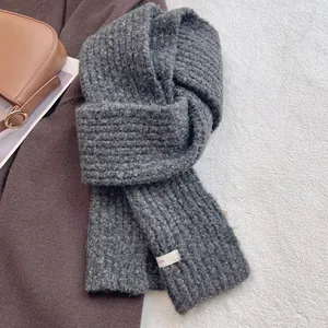Detailed view of dark grey chunky wool blend knit scarf with white woven brand label